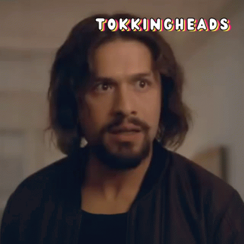 A Man With Long Hair And A Beard Is Looking At The Camera With The Words Tokingheads Above Him GIF