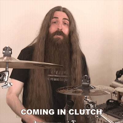 A Man With Long Hair And A Beard Is Playing Drums And The Words Coming In Clutch Are Above Him GIF