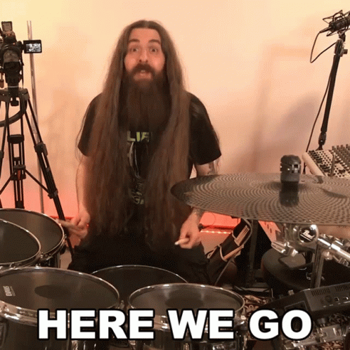 A Man With Long Hair And A Beard Is Playing Drums With The Words Here We Go Behind Him GIF