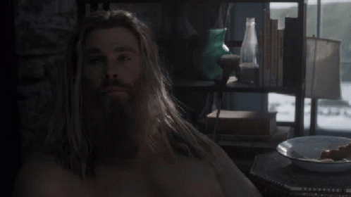 A Man With Long Hair And A Beard Is Sitting At A Table Eating Food . GIF