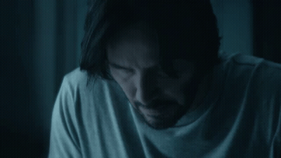 A Man With Long Hair And A Beard Is Sitting In A Dark Room . GIF