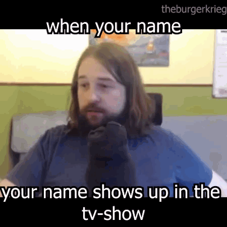 A Man With Long Hair And A Beard Is Sitting In Front Of A Tv And Talking On A Cell Phone . GIF