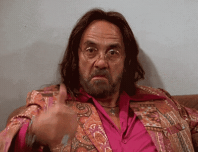 A Man With Long Hair And A Beard Is Sitting On A Couch And Giving A Thumbs Up GIF