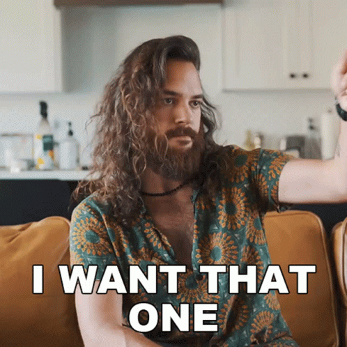 A Man With Long Hair And A Beard Is Sitting On A Couch And Saying " I Want That One " GIF
