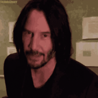 A Man With Long Hair And A Beard Is Smiling And Looking At The Camera GIF