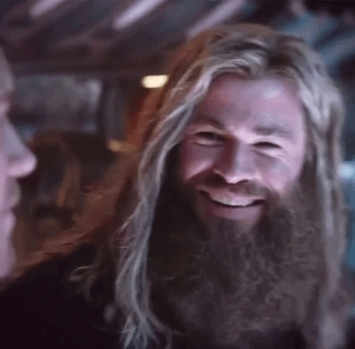 A Man With Long Hair And A Beard Is Smiling While Looking At Another Man . GIF