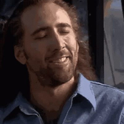 A Man With Long Hair And A Beard Is Smiling With His Eyes Closed In A Blue Shirt . GIF
