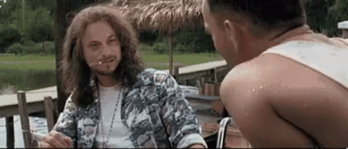 A Man With Long Hair And A Beard Is Smoking A Cigarette While Sitting Next To Another Man . GIF