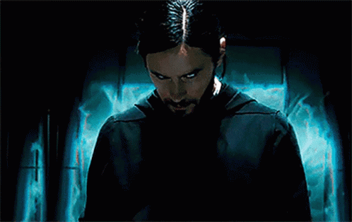 A Man With Long Hair And A Beard Is Standing In Front Of A Blue Wall . GIF