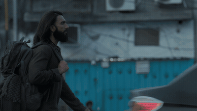 A Man With Long Hair And A Beard Is Standing In Front Of A Building GIF