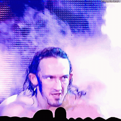 a man with long hair and a beard is standing in front of a crowd and smoke is coming out of his head .