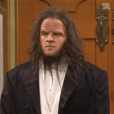 A Man With Long Hair And A Beard Is Standing In Front Of A Door . GIF