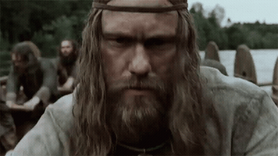 A Man With Long Hair And A Beard Is Standing In Front Of A Group Of Men In A Boat . GIF