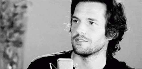 A Man With Long Hair And A Beard Is Standing In Front Of A Microphone In A Black And White Photo . GIF
