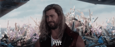 A Man With Long Hair And A Beard Is Standing In Front Of A Pile Of Flowers And Says Pfft GIF