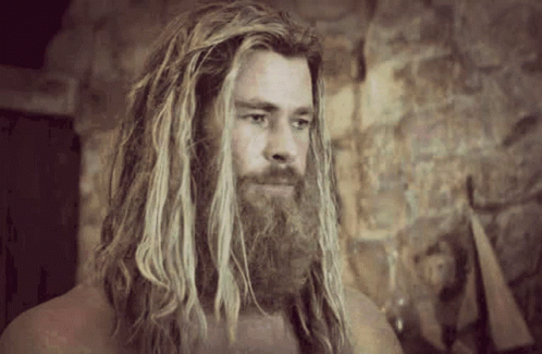 A Man With Long Hair And A Beard Is Standing In Front Of A Stone Wall In A Room . GIF