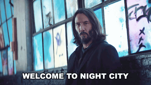 A Man With Long Hair And A Beard Is Standing In Front Of A Wall That Says Welcome To Night City On It GIF