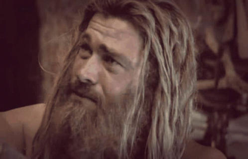 A Man With Long Hair And A Beard Is Standing In Front Of A Wall . GIF