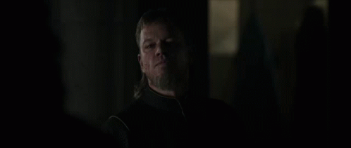 A Man With Long Hair And A Beard Is Standing In The Dark Looking At Something . GIF
