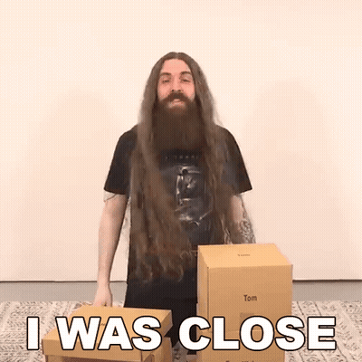 A Man With Long Hair And A Beard Is Standing Next To Boxes And Says I Was Close GIF