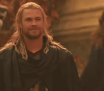 A Man With Long Hair And A Beard Is Wearing A Black Cape And Smiling . GIF