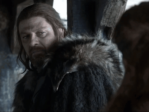 A Man With Long Hair And A Beard Is Wearing A Black Fur Coat GIF