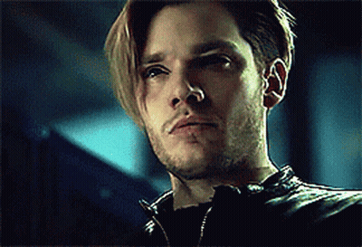 A Man With Long Hair And A Beard Is Wearing A Black Leather Jacket And Looking At The Camera . GIF