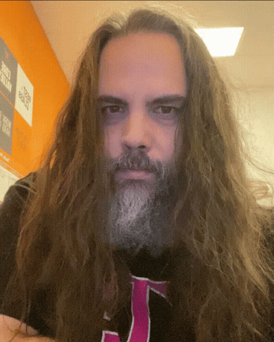 A Man With Long Hair And A Beard Is Wearing A Black Shirt With A Pink J On It GIF