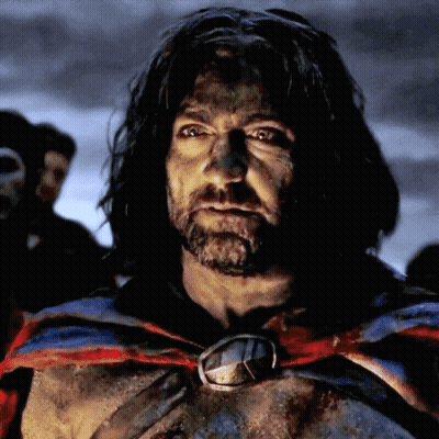 A Man With Long Hair And A Beard Is Wearing A Cape And A Medallion Around His Neck GIF