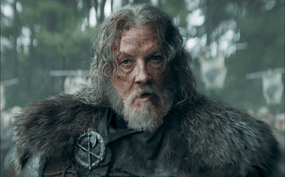 A Man With Long Hair And A Beard Is Wearing A Fur Coat And A Badge With A Cross On It GIF