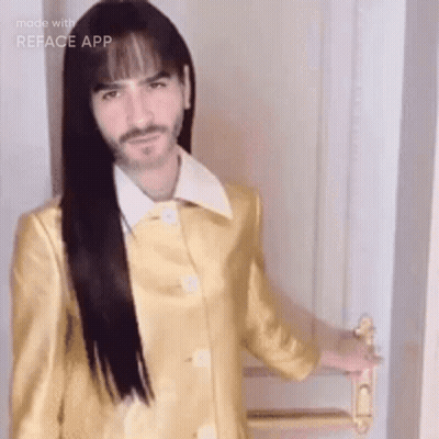 A Man With Long Hair And A Beard Is Wearing A Yellow Coat And Holding A Door Handle . GIF