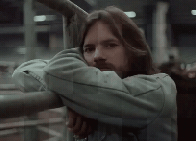 A Man With Long Hair And A Beard Leans Against A Metal Railing . GIF