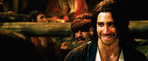 A Man With Long Hair And A Beard Smiles In Front Of A Crowd GIF