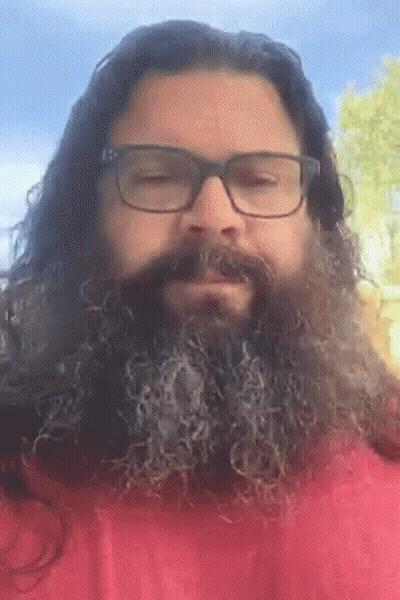 a man with long hair and a beard wearing glasses and a red shirt
