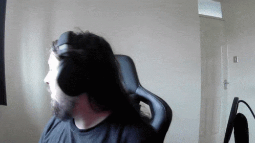 A Man With Long Hair And A Beard Wears Headphones While Sitting In A Chair GIF