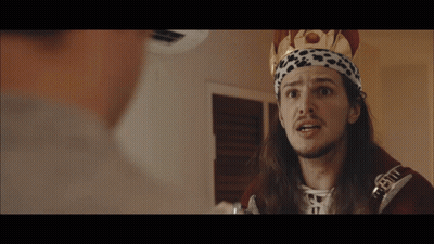 a man with long hair and a crown on his head is talking to another person