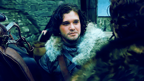 A Man With Long Hair And A Fur Collar Is Talking To Another Man GIF