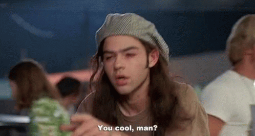 A Man With Long Hair And A Hat Is Sitting At A Table And Talking To Another Man . GIF