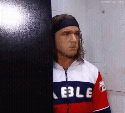 A Man With Long Hair And A Headband Is Leaning Against A Wall In A Room . GIF