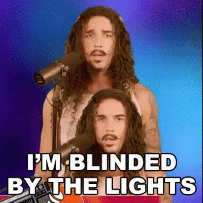 A Man With Long Hair And A Mustache Is Singing Into A Microphone And Says I 'M Blinded By The Lights GIF
