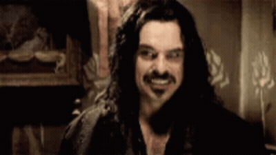 A Man With Long Hair And A Mustache Is Smiling And Looking At The Camera . GIF
