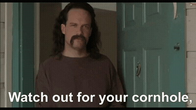 A Man With Long Hair And A Mustache Is Standing In Front Of A Door And Says " Watch Out For Your Cornhole " GIF
