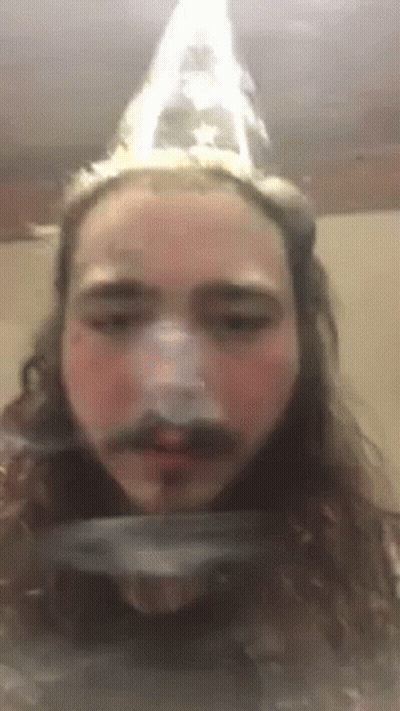 A Man With Long Hair And A Mustache Is Wearing A Cone Hat . GIF