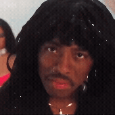 A Man With Long Hair And A Mustache Is Wearing A Wig And A Necklace . GIF