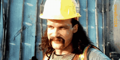 A Man With Long Hair And A Mustache Wearing A Hard Hat With The Year 2004 On The Bottom Right GIF