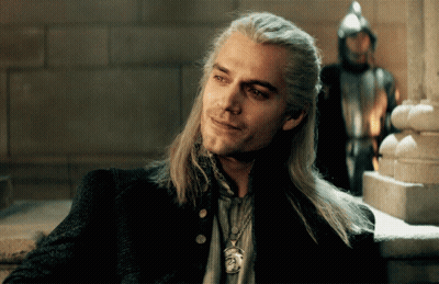 A Man With Long Hair And A Necklace With A Lion On It Smiles GIF