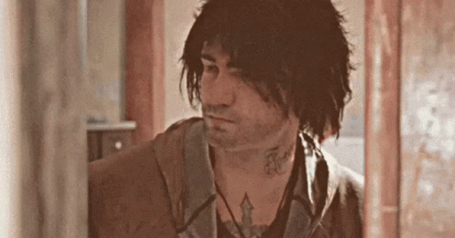 A Man With Long Hair And A Tattoo On His Neck Is Standing In A Room . GIF