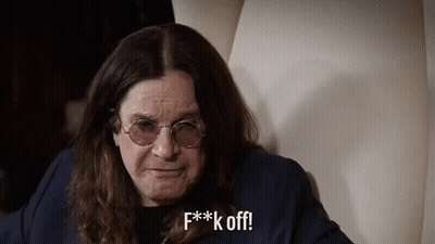 A Man With Long Hair And Glasses Is Sitting On A Chair And Making A Funny Face . GIF