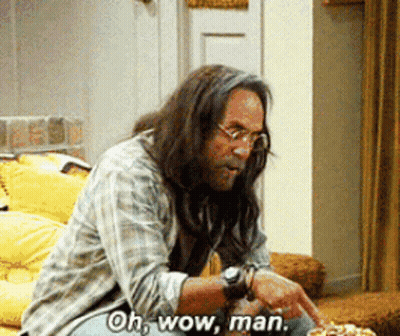 A Man With Long Hair And Glasses Is Sitting On A Couch And Says Oh Wow Man GIF