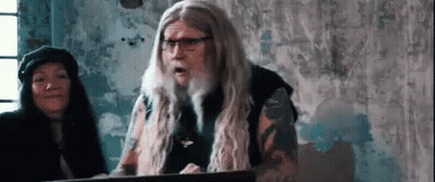 a man with long hair and glasses is standing in front of a podium .